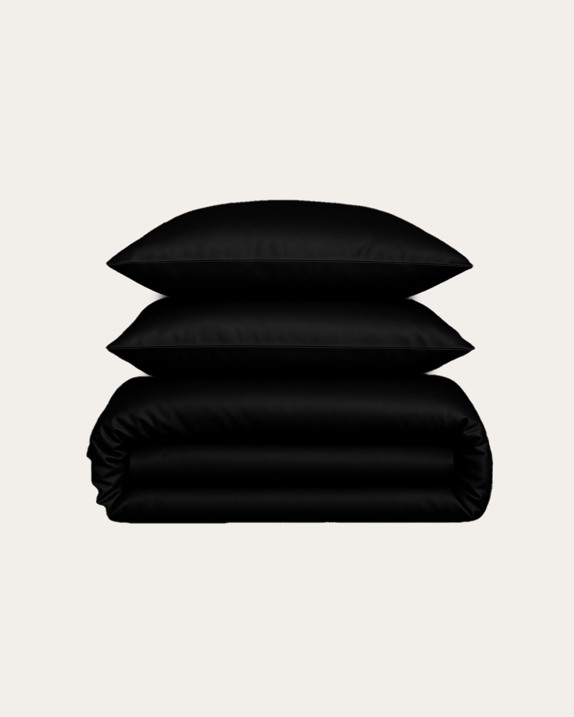 Black velour satin bedding set featuring stacked pillows and a rolled duvet for modern bedroom elegance.