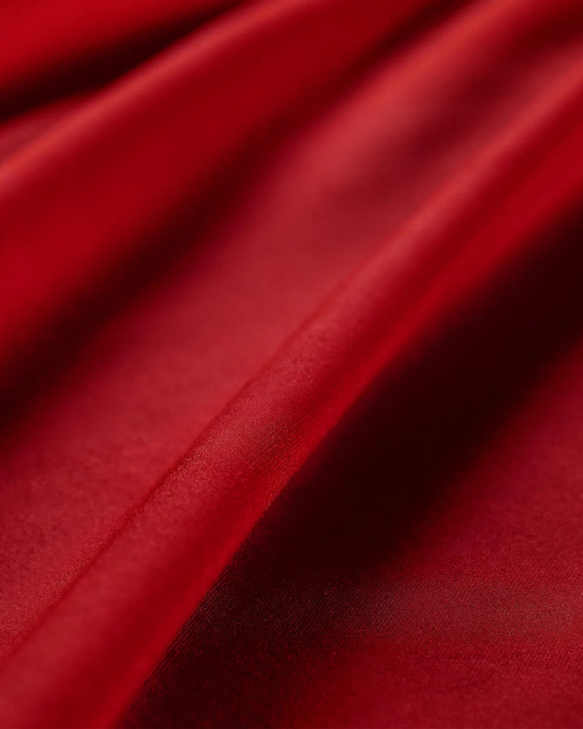 Close-up of luxurious red satin fabric, showcasing its smooth texture and vibrant color for a pillowcase.